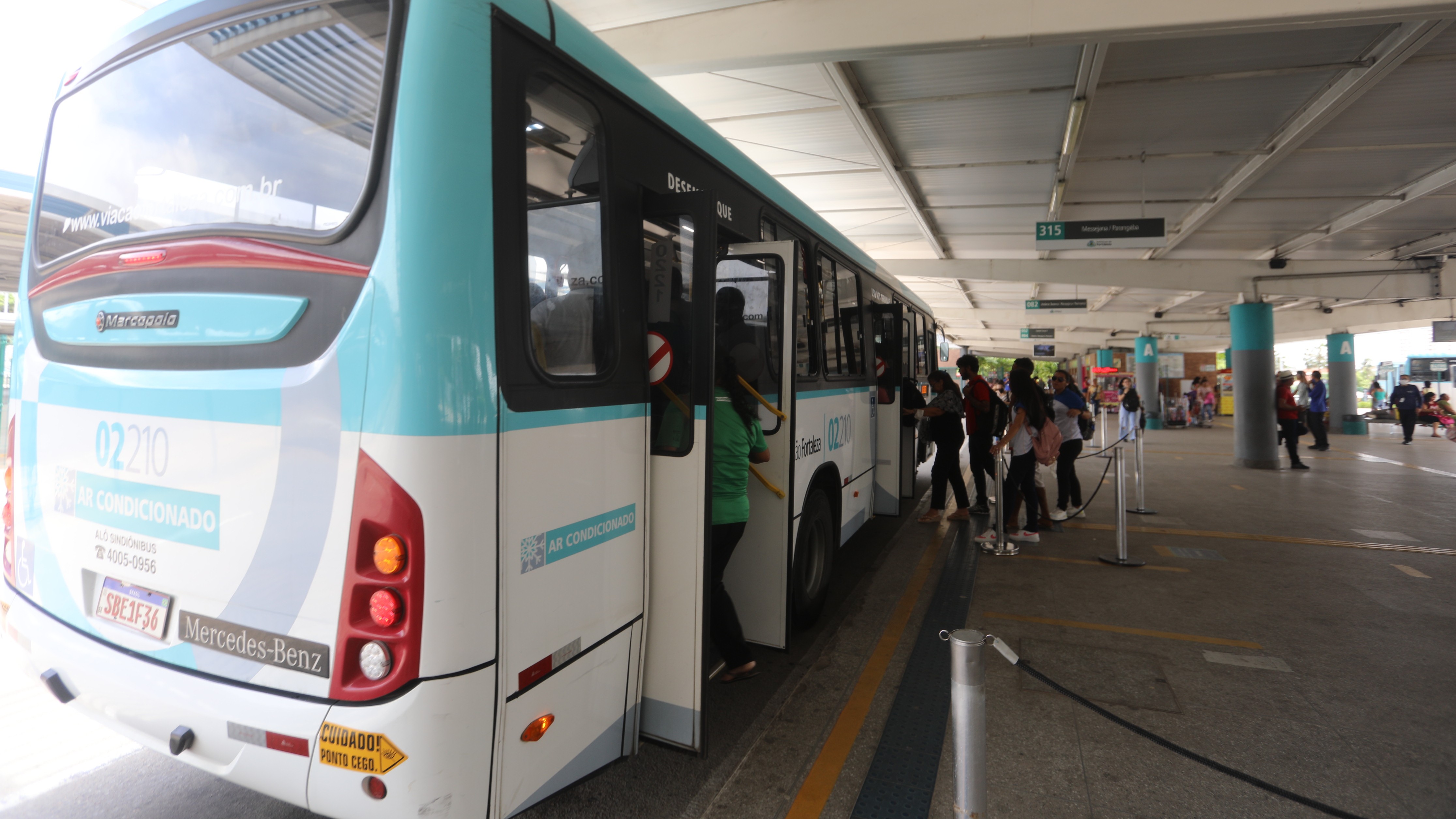 pessoas embarcando num ônibus numa plataforma de terminal de transporte